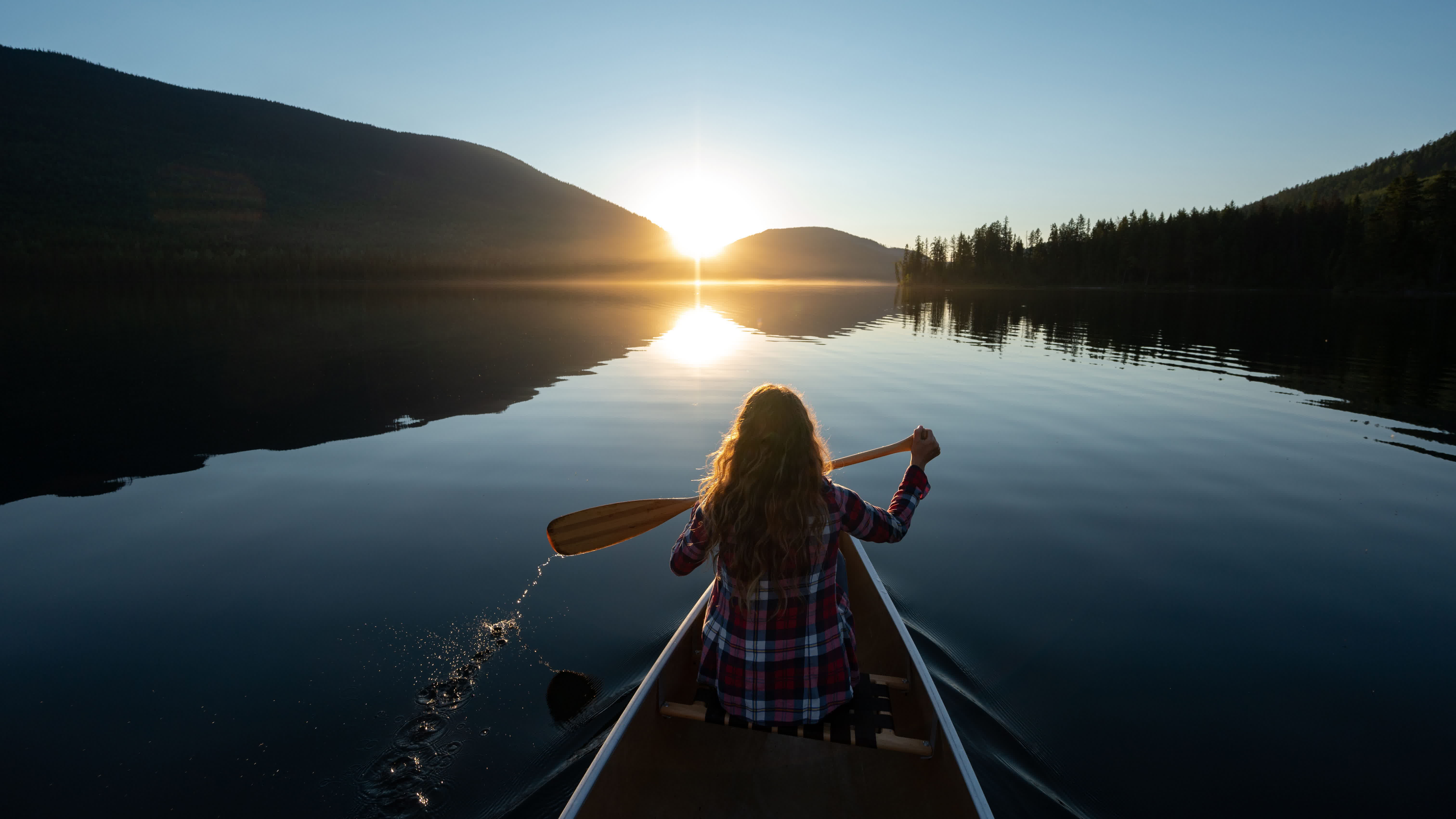 Mujer remando en canoa en un impresionante lago de montaña